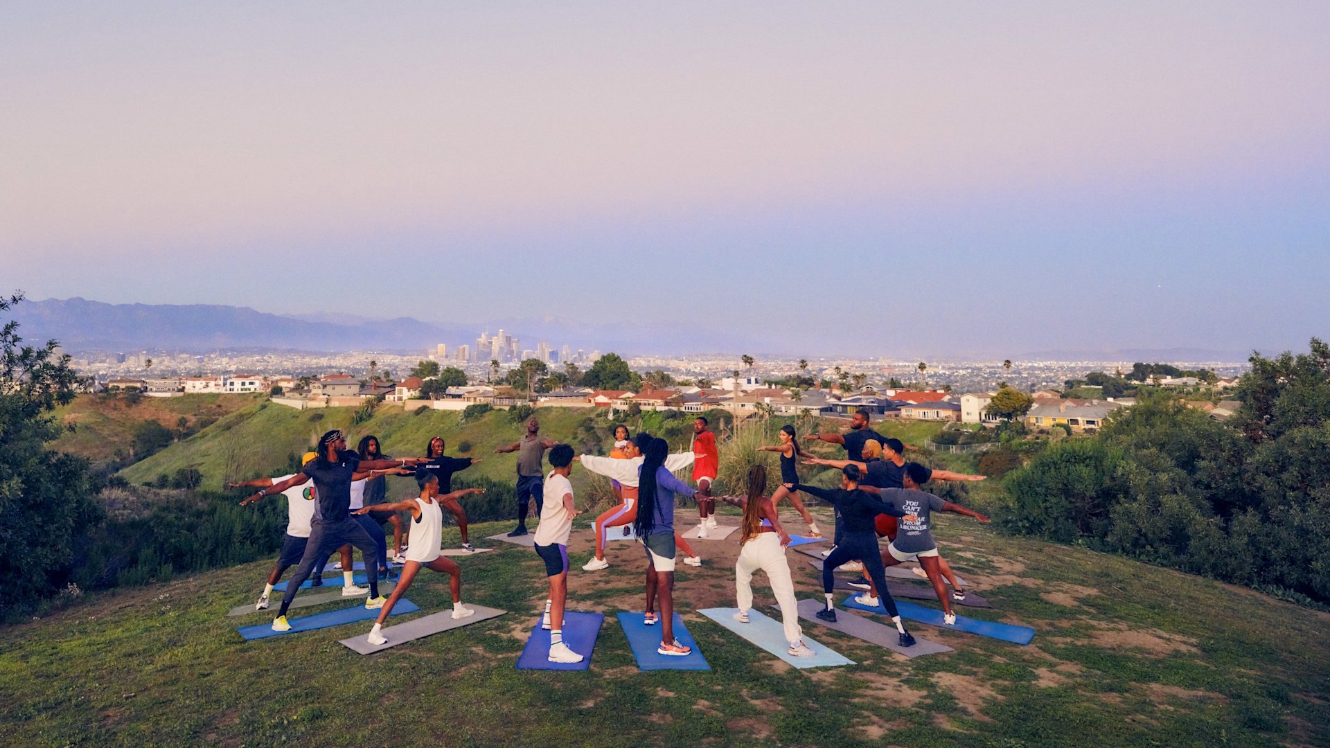 A group of people doing yoga poses on a hilltop, with a city in the distance.